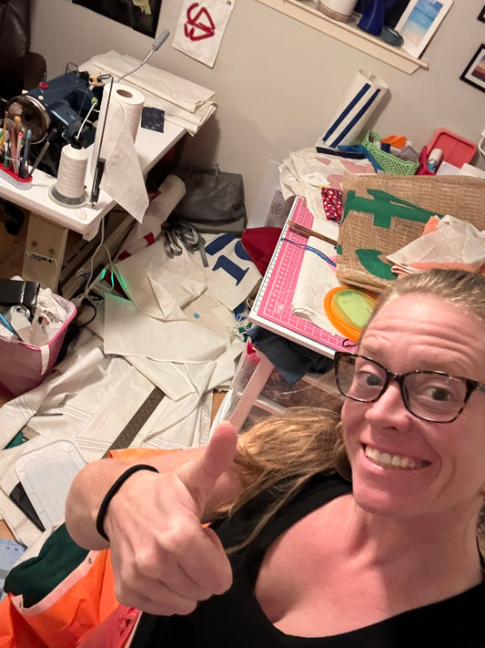 Coco in her studio surrounded by cut sailcloth and works in progress, giving a thumbs up